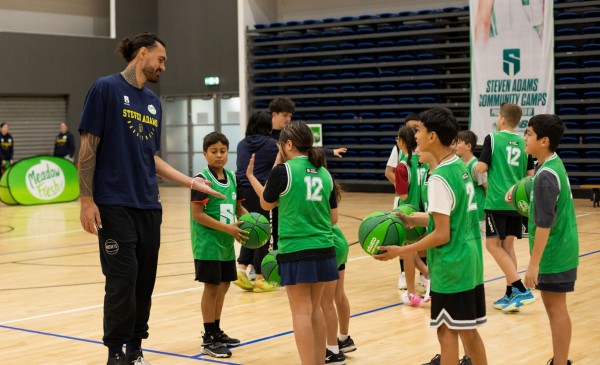 Steven Adams giving kids high fives as they play basketball at his camp